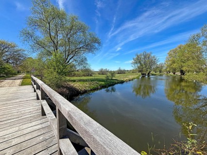 A quiet river flows under a blue sky next to a wooden bridge and green trees, Gartow, Lower Saxony,