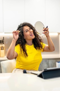 Vertical photo of a happy latin woman making up alone sitting in the kitchen smiling at the camera