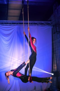 Two trapeze artists performers execute an elegant aerial routine on ropes, dressed in shiny black