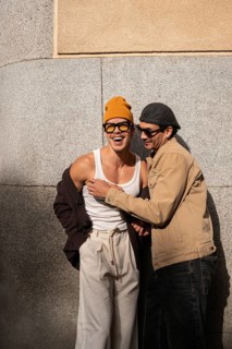 A Colombian gay couple laughing together in casual attire against an urban backdrop. Capturing