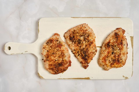 Three cooked pork chops placed on white wooden cutting board ready for eating. Chops show golden
