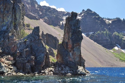 Steep rocks on the edge of a lake with dramatic mountain scenery in the background, Crater Lake