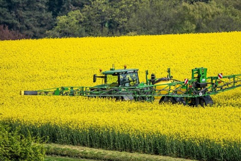 Agriculture, rapeseed field in full bloom, farmer sprays the field with a John Deere M952 trailer