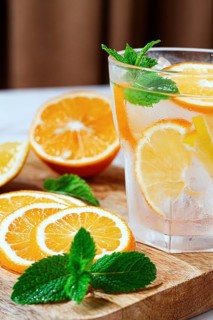 Slices of orange and mint leaves sit next to a clear glass filled with a refreshing drink. The