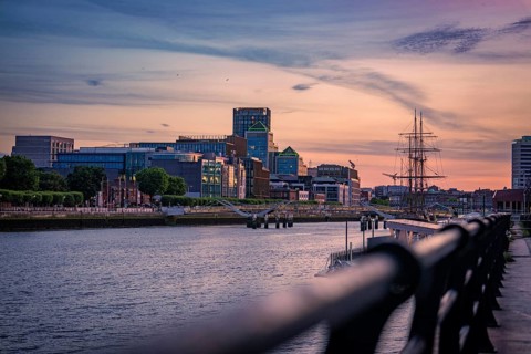 Urban skyline at sunset with river and historic sailing ship in the foreground, Dublin, Ireland