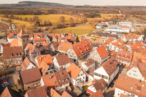 Overview of a historic town with half-timbered architecture and red roofs, surrounded by fields,