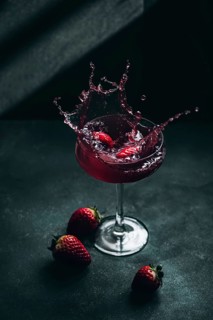 A dynamic image of strawberry liqueur splashing in a glass. Fresh strawberries accent the dark