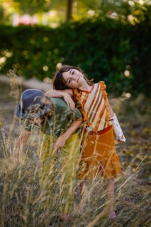 Two children enjoy a sunny day in a meadow, surrounded by tall grass and lush greenery. The moment