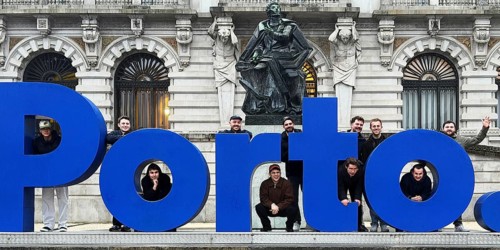 Large, blue postage lettering in front of the town hall with men posing, group photo in front of