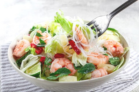 Thai salad with shrimp and rice noodles, pineapple slices, coriander and mint leaves, on a white