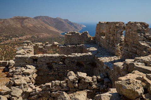 Ancient ruins on a hill with views of mountains and the sea, surrounded by clear blue sky,