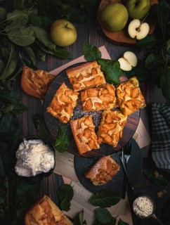 Sliced apple pie on wooden board, apples, leaves, whipped cream, from above, food photography