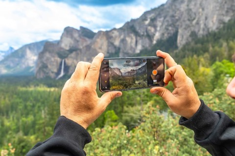 Hands holding a smartphone capturing the iconic tunnel view panorama of yosemite valley, featuring
