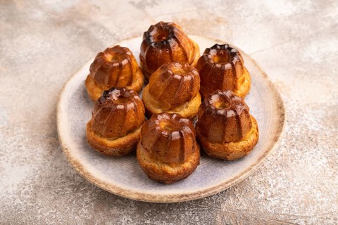 Golden caramelized Canele cookies dessert, cup of coffee, on brown concrete background, close up,