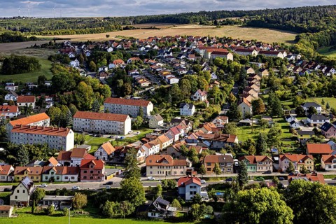 A picturesque village with numerous houses, surrounded by green meadows and hills under a cloudy