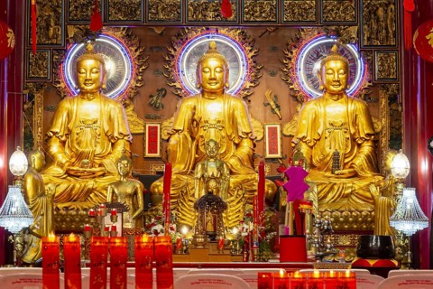 A quiet moment in the heart of a Chinese-Buddhist temple: Three golden Buddha figures shine in warm