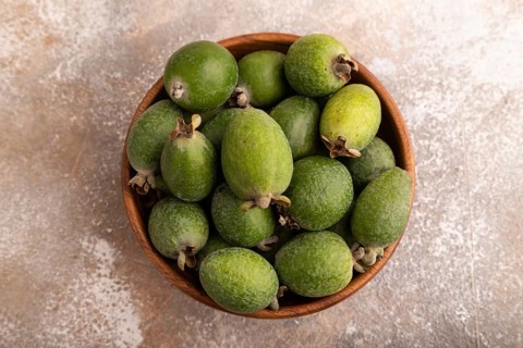 Ripe Feijoa in wooden bowl on brown concrete background, top view, flat lay, close up, minimalism