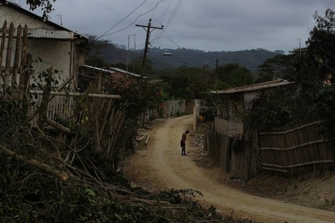 A person on a sandy road in a village with wooden fences, cloudy sky, San Lorenzo, Ecuador