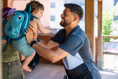 Father holding his young son with a playful backpack after school, sharing a moment of happiness