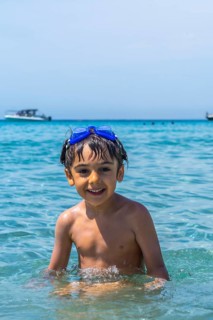 Happy little boy wearing swimming goggles, smiling directly at the camera while standing in the