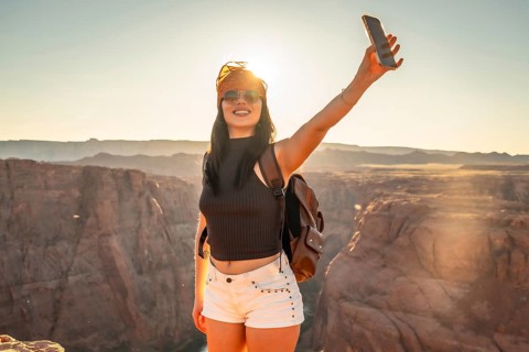 Young woman smiling and holding a smartphone, capturing a selfie against the vast desert canyon