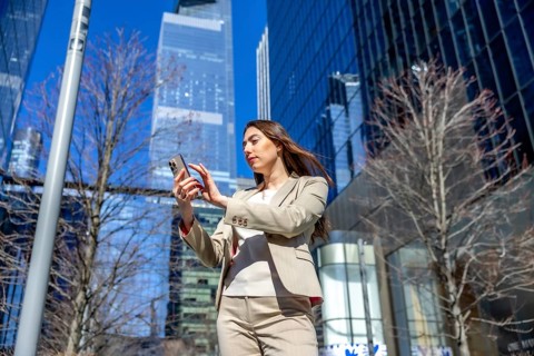 Businesswoman looking at her mobile phone, navigating or scrolling content outdoors in a modern