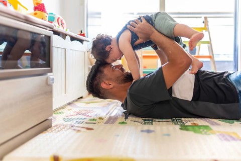 Father lifts his baby son during playful floor time, sharing a joyful, affectionate bonding moment