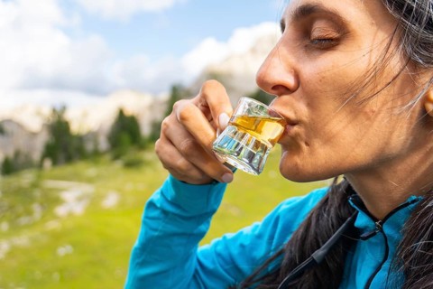 Close up woman traveler drinking local herbal spirit schnapps or grappa shot glass wooden terrace