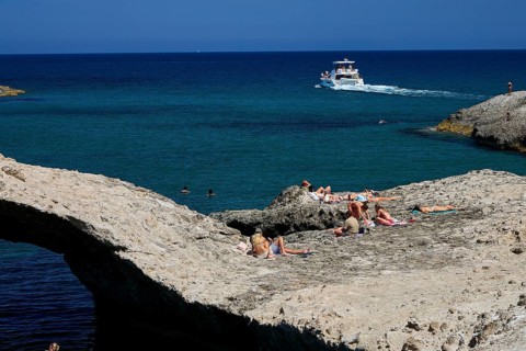People sunbathe on rocky water's edge while a boat passes by, Kapras, Kapros, Beach, Kapros Beach,