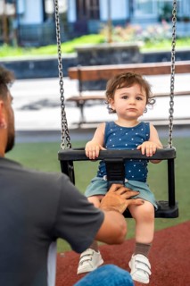 Father pushes young son on a park swing, sharing joyful outdoor bonding moment that captures
