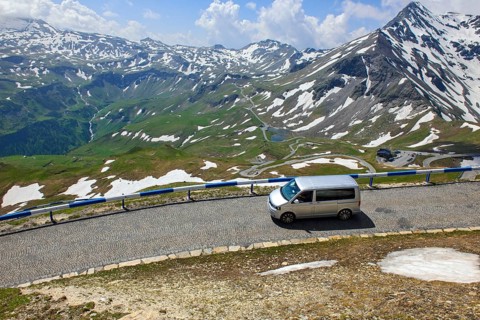 Mini-van VW bus drives on historic alpine road with cobblestones on driveway access to the