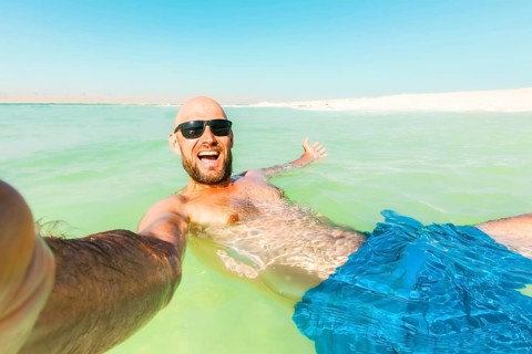 POV caucasian male Man floating wave pose send greetings in turquoise Dead Sea water wearing a