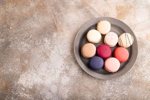 Macarons colourful cookies dessert, on brown concrete background, copy space, top view, flat lay