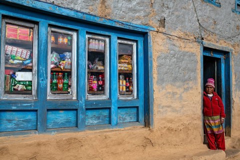 An elderly woman from the Sherpa ethnic group stands in the front door to a small shop on the way