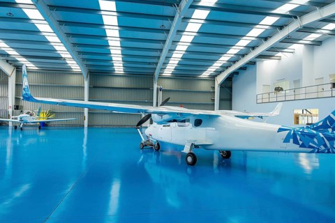 Two small propeller airplanes parked inside a spacious, clean, and bright hangar with a striking