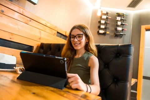 Young woman wearing glasses and a green sleeveless top, smiling while using a tablet computer on a