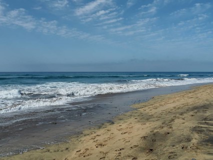 Waves roll in on the beach, footprints run along the water under cloudy sky, Maspalomas dunes, Gran