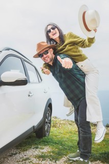 Portrait Happy couple Man with woman having fun piggyback next to white car on coastal cliff. Vast