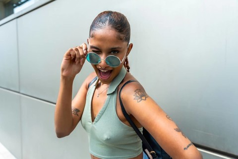 Young woman showing playful expression and winking, pulling down her sunglasses while happily