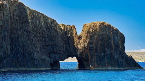 A large rock formation juts out of the blue sea, with a clear blue sky, Glaronisia, Glaronesia,