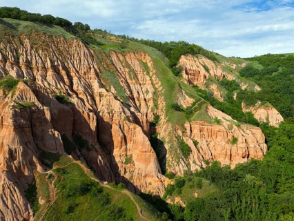 Red rock formations in green landscape with lush vegetation and erosion patterns, aerial view, Râpa