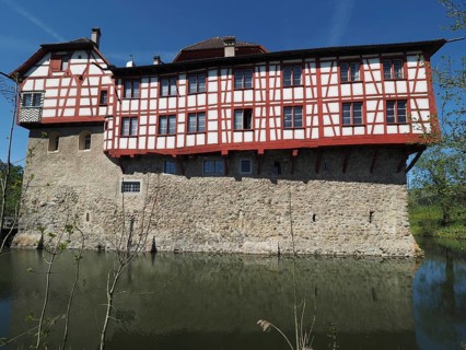 Half-timbered building in castle structure, surrounded by a moat and clear skies, Hagenwil,