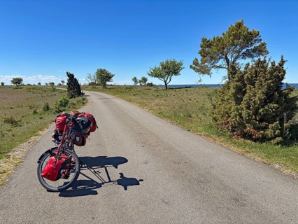 Lonely country road with parked bike and red bags under clear blue sky, cycle tourism, Sandvik,