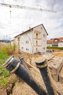 Residential building in a construction site with exposed pipes and cranes in the background,