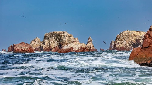 Rock formations in the sea with strong waves under a blue sky, The rocky coast of the Islas