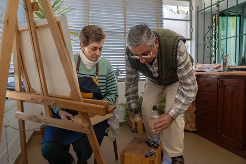 Senior man placing painting materials on a small table while preparing an art session with his wife