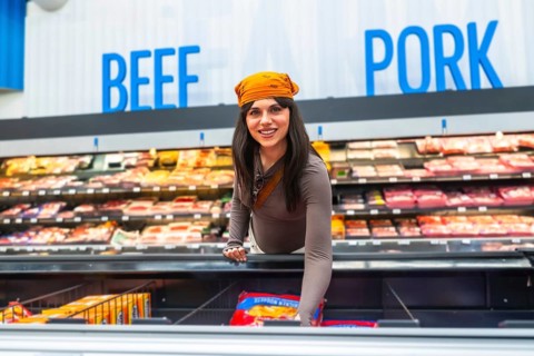Woman smiling, reaching for a package of frozen food in an open display freezer, with shelves of