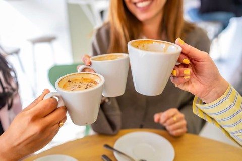 Three friends celebrating their friendship with a happy coffee toast, holding white cups filled