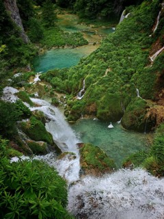 View from above of cascading waterfalls and turquoise-blue lakes amidst thick green vegetation and