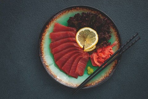 Fresh tuna sashimi served with lemon, wasabi, and pickled ginger on a dark background